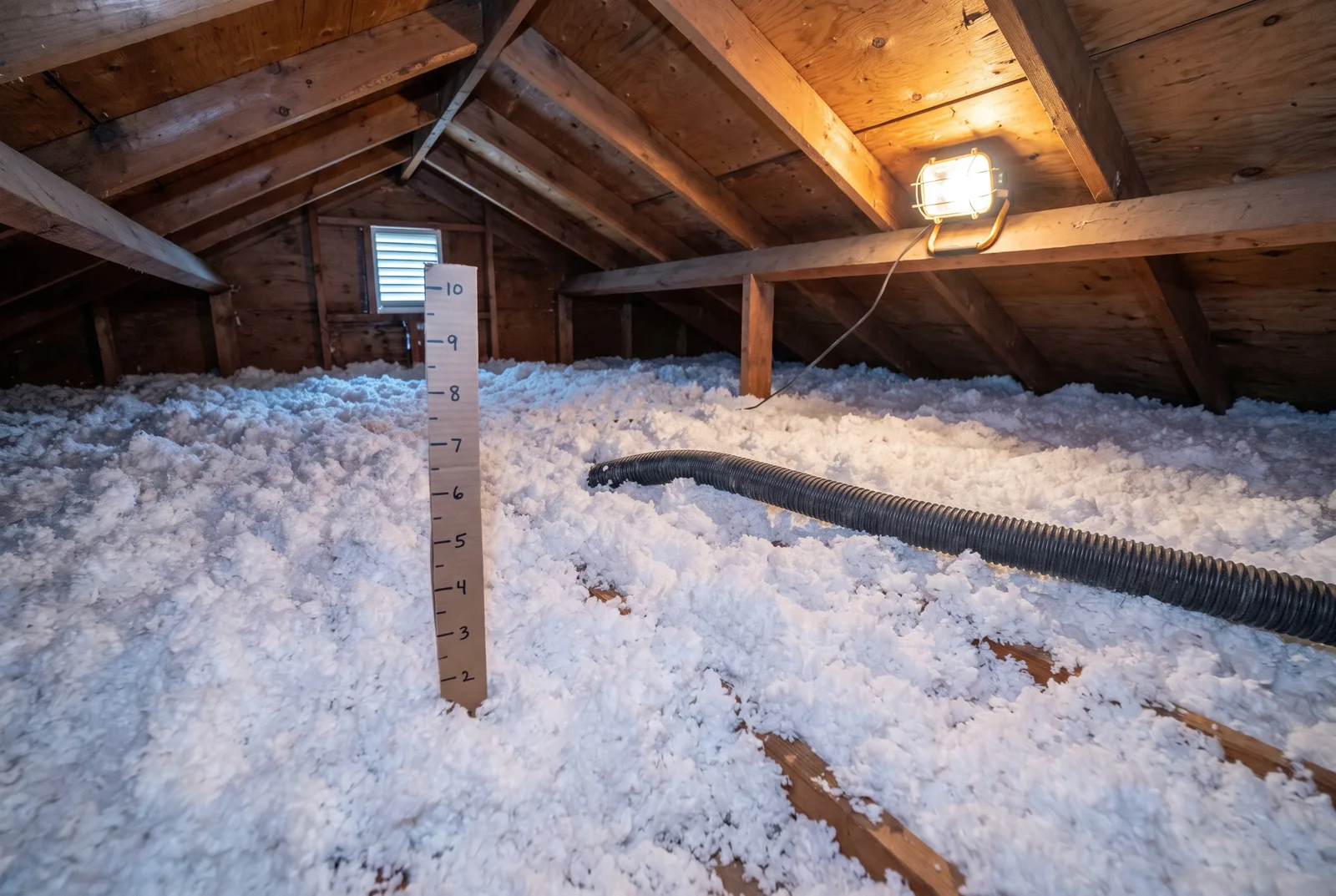 Fresh blown-in fiberglass insulation covering an attic floor with the blower hose